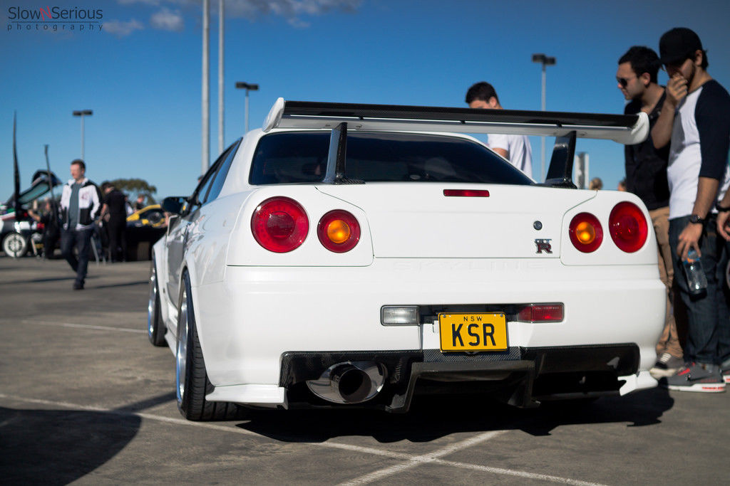 Rear view of a white Nissan Skyline R34 with large rear wing at a car meet