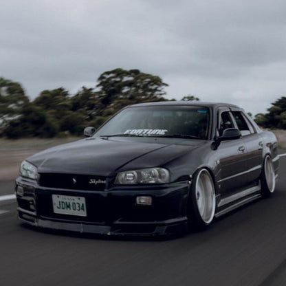 Black Nissan Skyline R34 fitted with JSAI Aero body kit driving on road front view