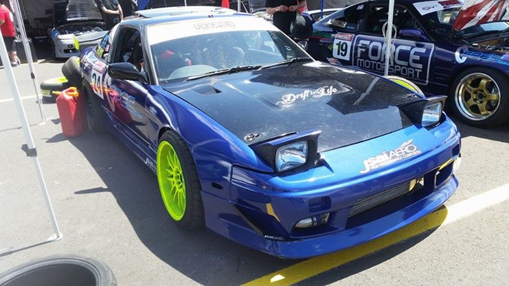 Front side view of a blue Nissan 180SX drift car with JSAI Aero front bar, pop-up headlights, and neon green wheels