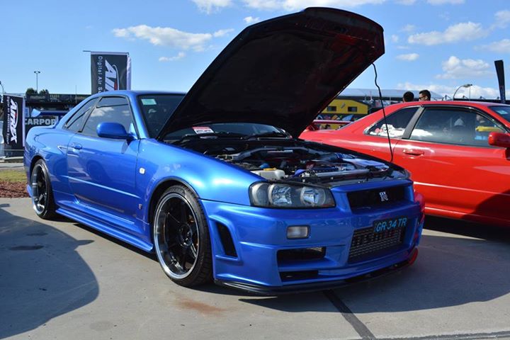 Blue Nissan Skyline R34 with JSAI Aero body kit and open hood at car show