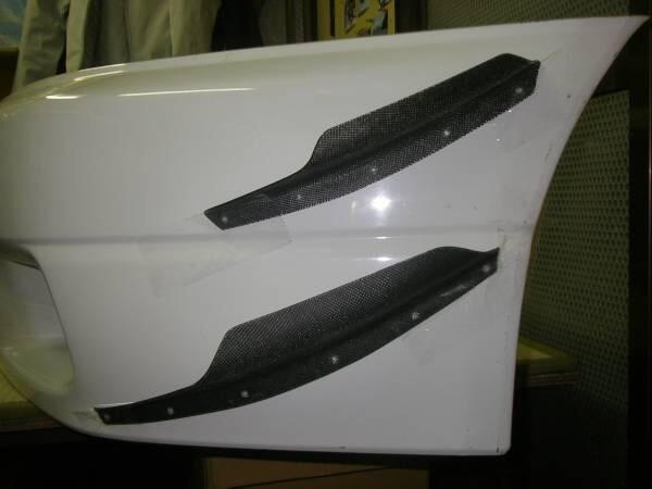 White performance car front bumper with carbon fibre canards mounted on the side for improved aero flow