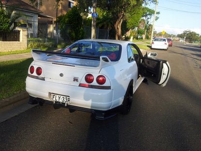 Rear angle view of white Nissan Skyline R33 GT-R parked on street with driver door open