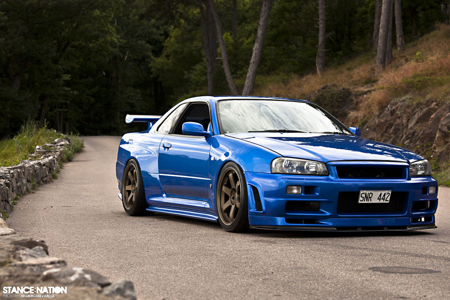 Front three-quarter view of blue Nissan Skyline R34 with aero body kit and GT wing