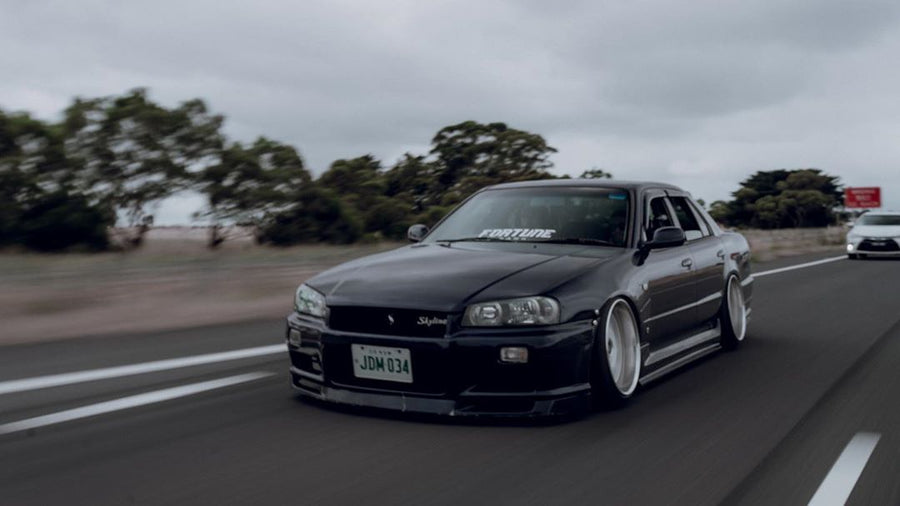 Black Nissan Skyline R34 with JSAI Aero body kit driving on highway front view