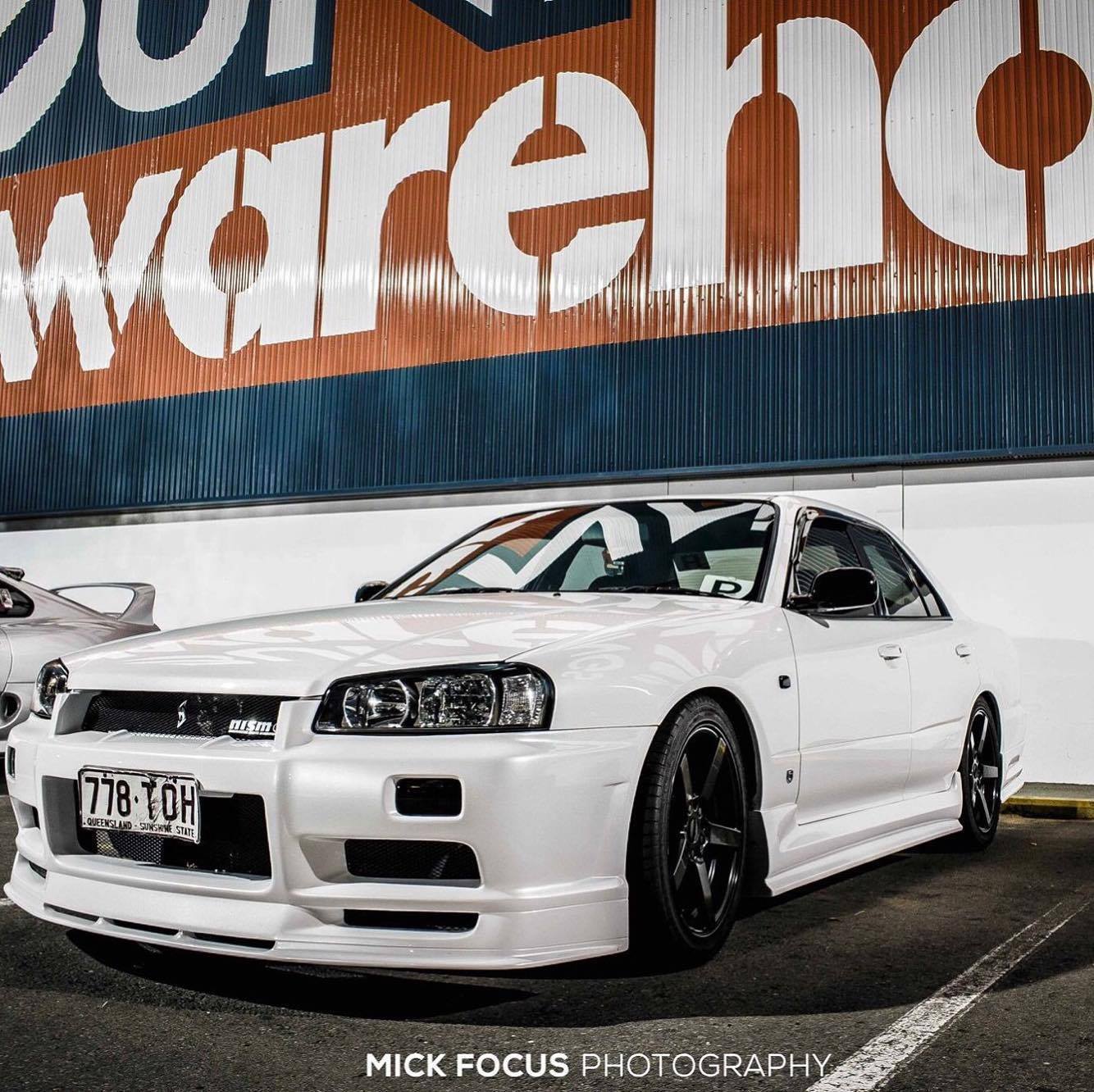 White Nissan Skyline R34 fitted with JSAI Aero body kit parked in industrial warehouse area