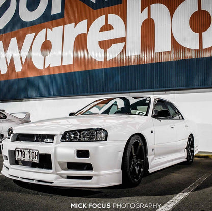 White Nissan Skyline R34 fitted with JSAI Aero body kit parked in industrial warehouse area