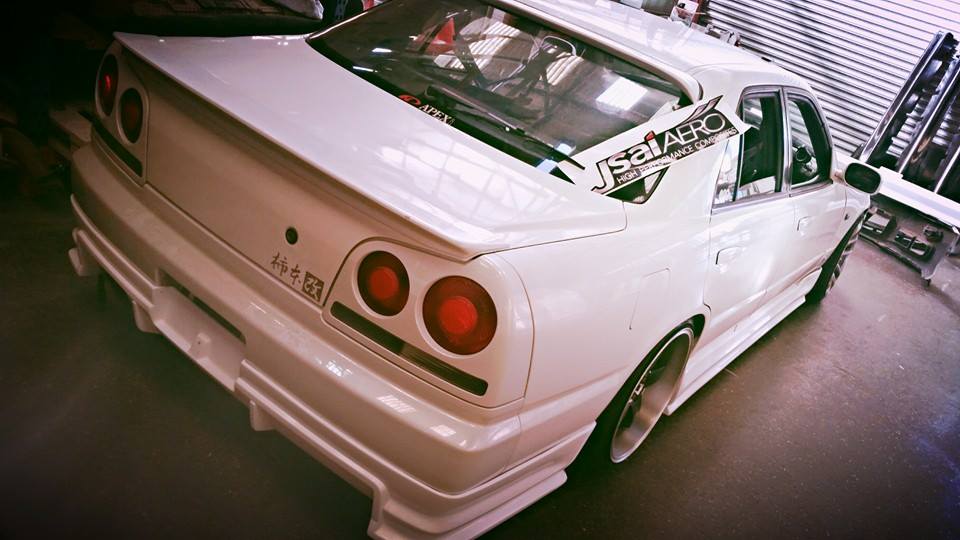 White Nissan Skyline R34 fitted with JSAI Aero rear body kit inside workshop rear view