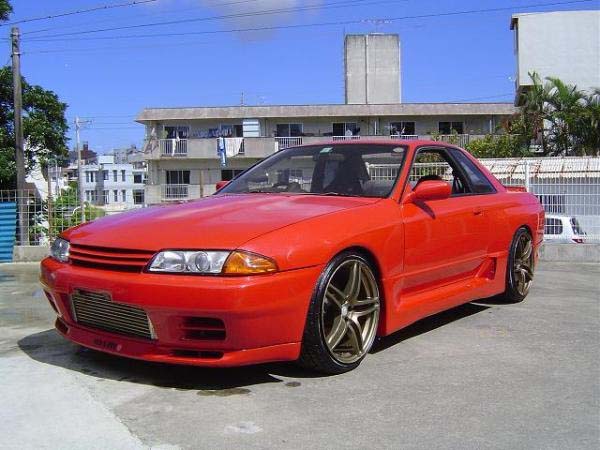 Front side view of a red Nissan Skyline R32 with aftermarket front bumper, intercooler, and bronze wheels