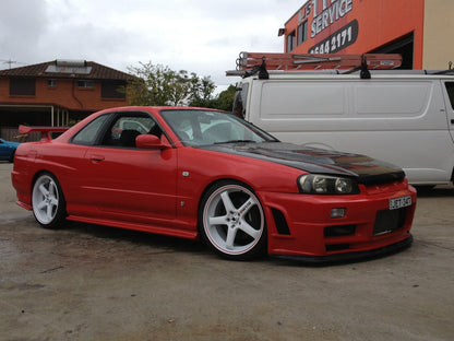 Red Nissan Skyline R34 with JSAI Aero body kit, front lip, side skirts, and aftermarket wheels