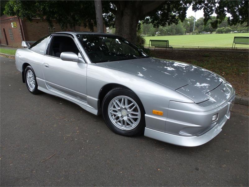 Front side view of a silver Nissan 180SX with front lip, side skirts, and factory-style wheels parked outdoors