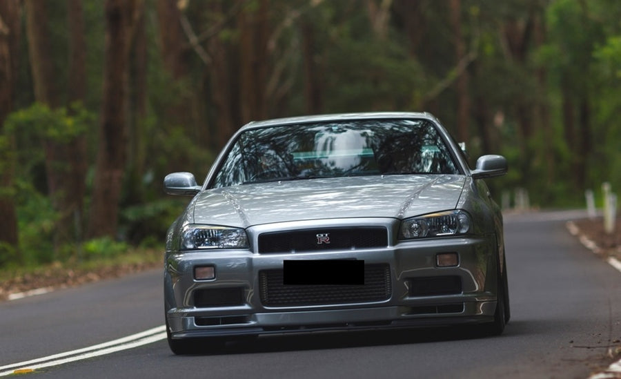 Front view of silver Nissan Skyline R34 with JSAI Aero body kit driving on forest road