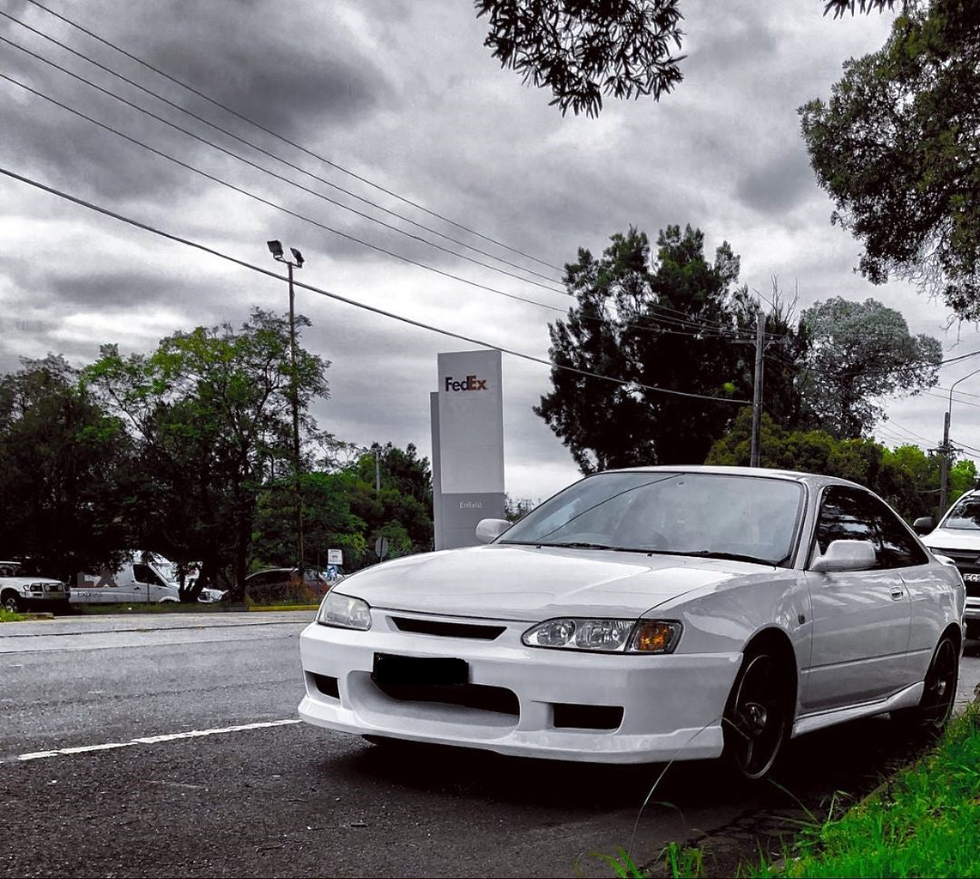 White Toyota AE111 Corolla Levin front view parked roadside, modified street build with aftermarket wheels and clean exterior styling