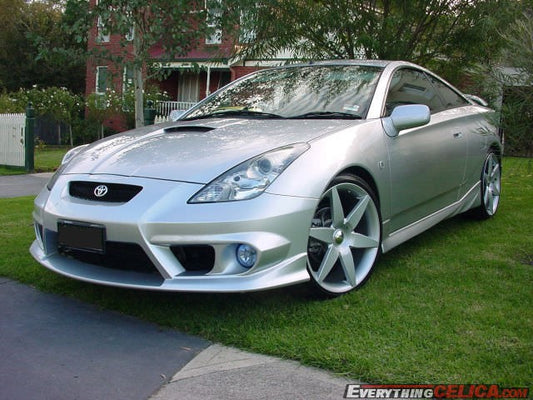 Silver Toyota Celica T23 with JSAI Aero front lip and side skirts aftermarket body kit front angle view on grass
