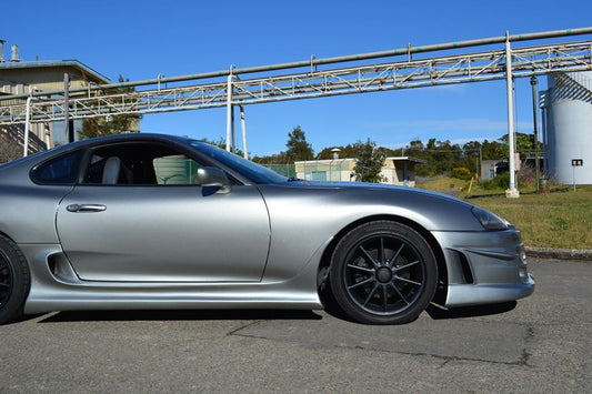 silver Toyota Supra JZA80 with Top Secret style side skirts and black wheels parked in industrial setting
