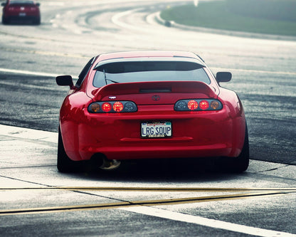 Red Toyota Supra rear view driving on road, modified performance car with wide stance and aftermarket exhaust