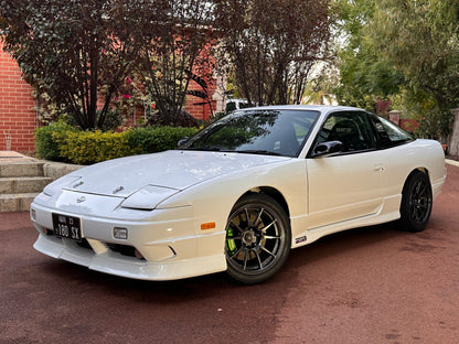 Front angle view of a white Nissan 180SX with front lip, side skirts, and black aftermarket wheels parked outdoors