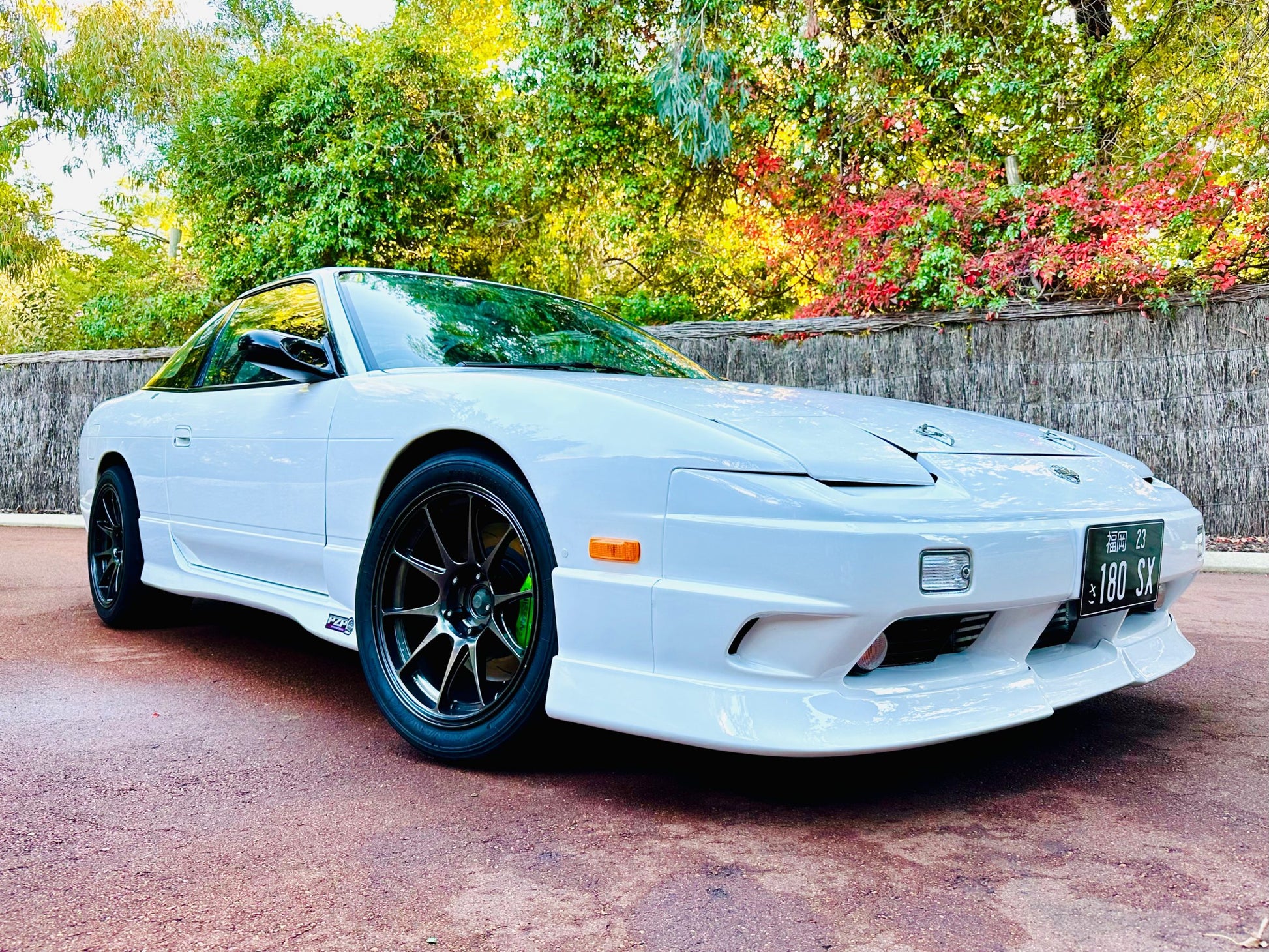 Front side view of a white Nissan 180SX with side skirts, front lip, and black aftermarket wheels parked outdoors