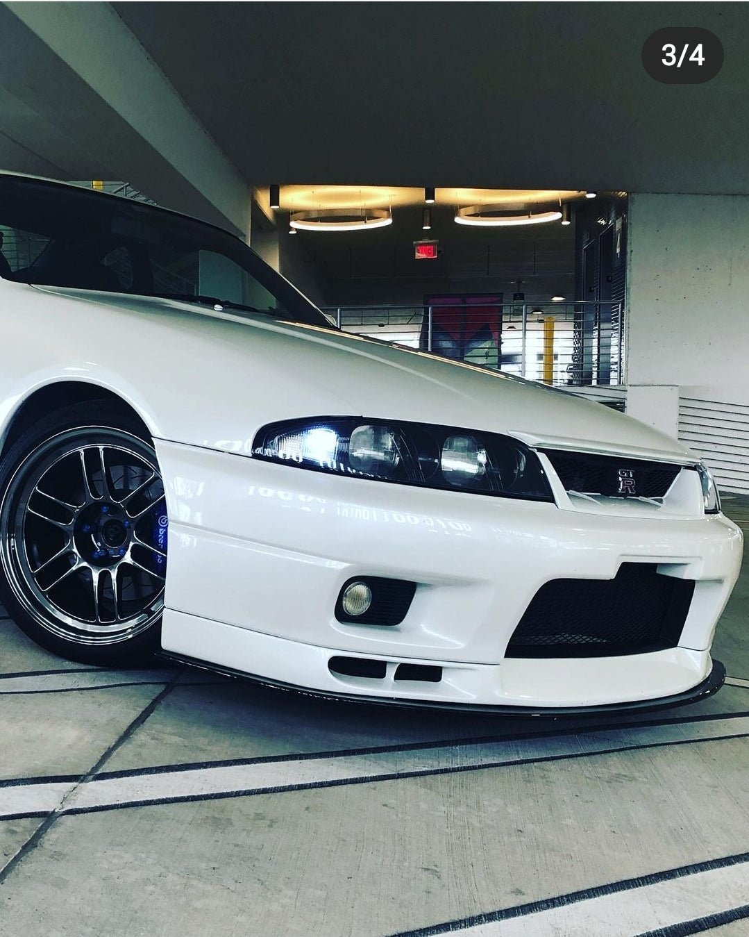 Close-up of a white Nissan Skyline R33 front bumper with front lip, fog light, and aftermarket wheel