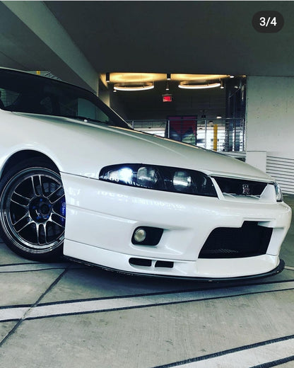 Close-up of a white Nissan Skyline R33 front bumper with front lip, fog light, and aftermarket wheel