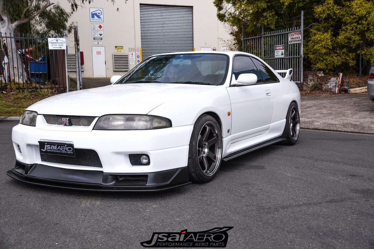 Front side view of a white Nissan Skyline R33 with JSAI Aero front lip, side skirts, and aftermarket wheels