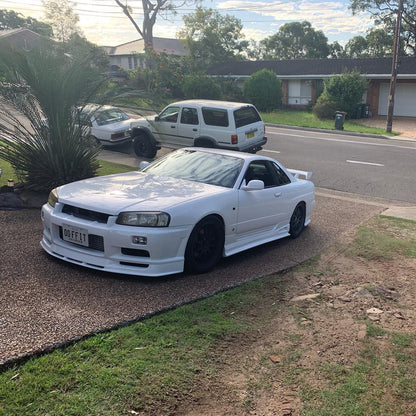 White Nissan Skyline R34 fitted with JSAI Aero body kit parked in residential driveway