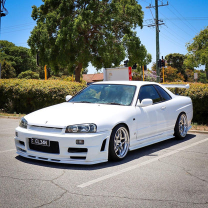 White Nissan Skyline R34 with JSAI aero front bumper and side skirts showcasing performance body kit and aggressive styling