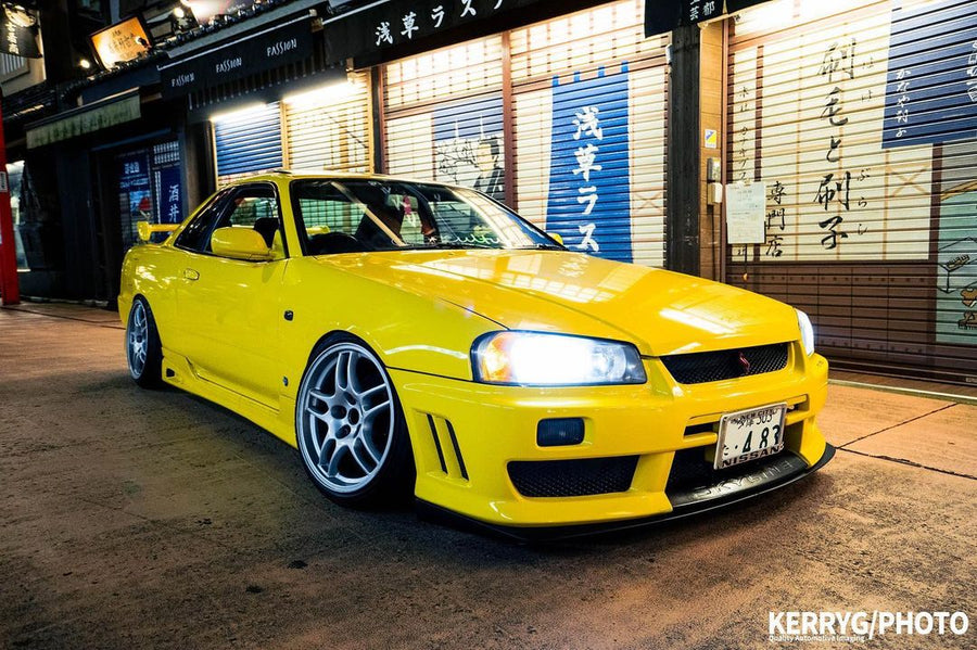 Yellow Nissan Skyline R34 with JSAI Aero body kit parked on city street at night front view